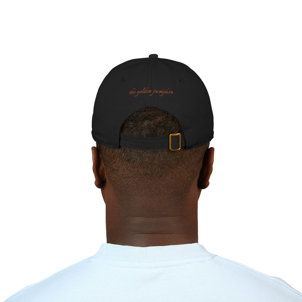 A male wearing a black baseball cap with text 'the golden pumpkin' on the back, in rusty orange color. The golden pumpkin is the store name.