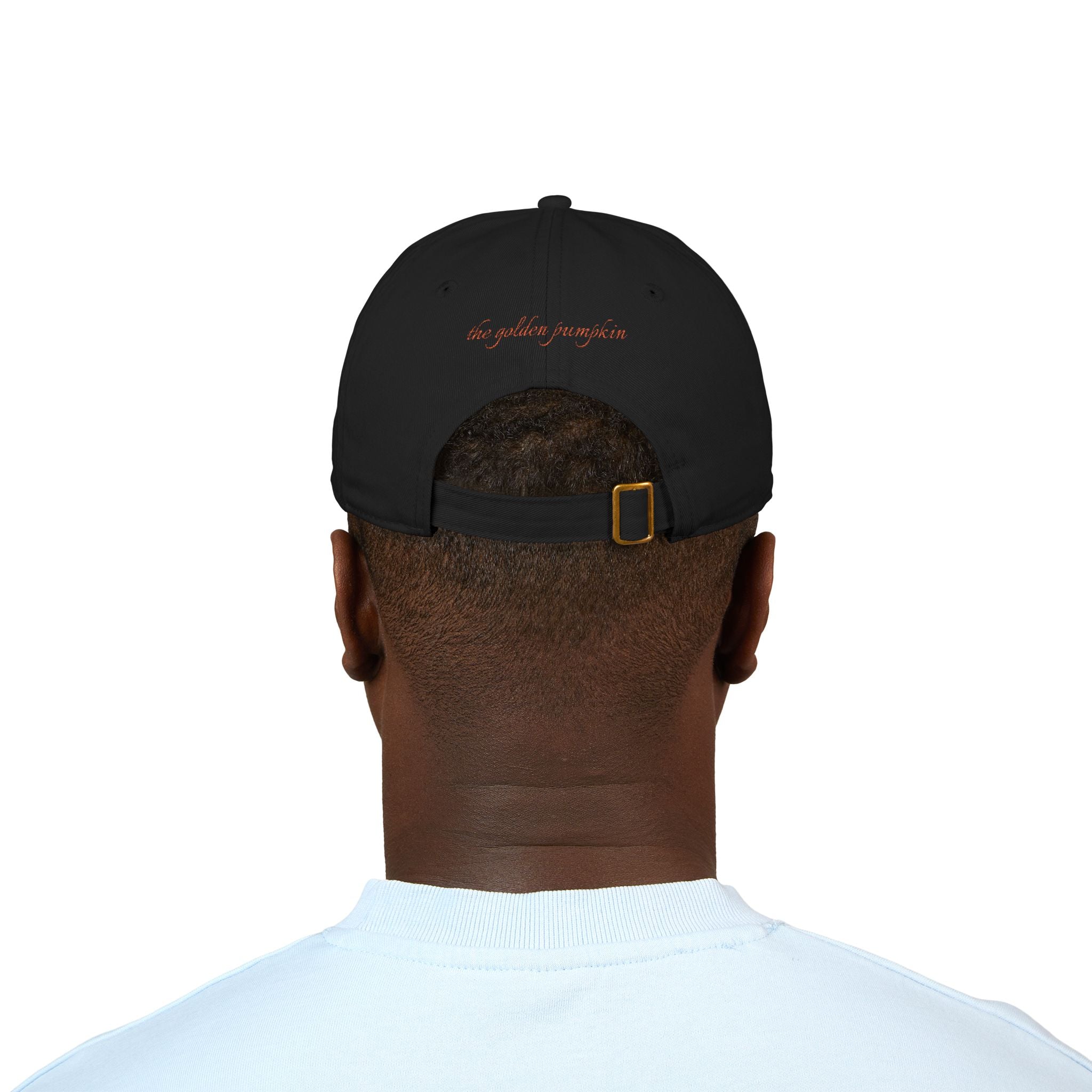 A male wearing a black baseball cap with text 'the golden pumpkin' on the back, in rusty orange color. The golden pumpkin is the store name.