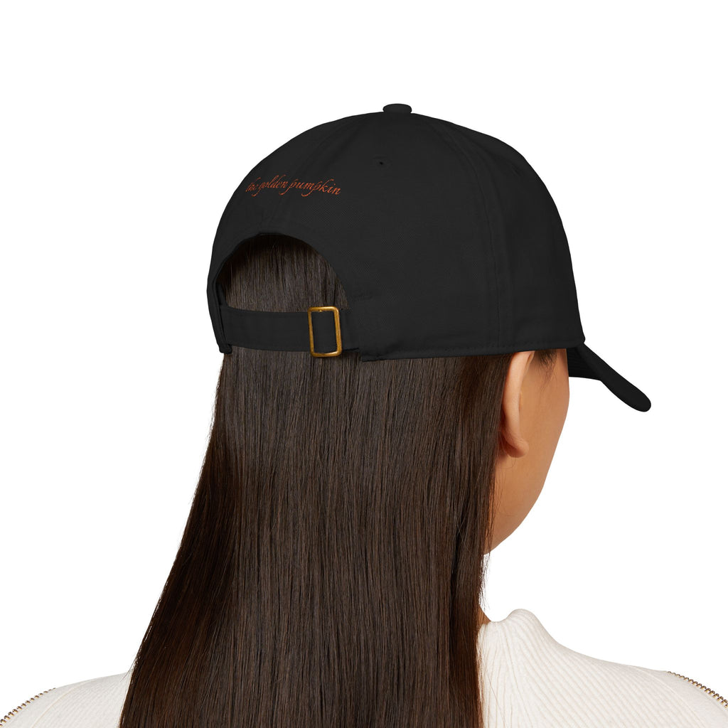 Female wearing a black baseball cap with text 'the golden pumpkin' on the back, in rusty orange color. The golden pumpkin is the store name.
