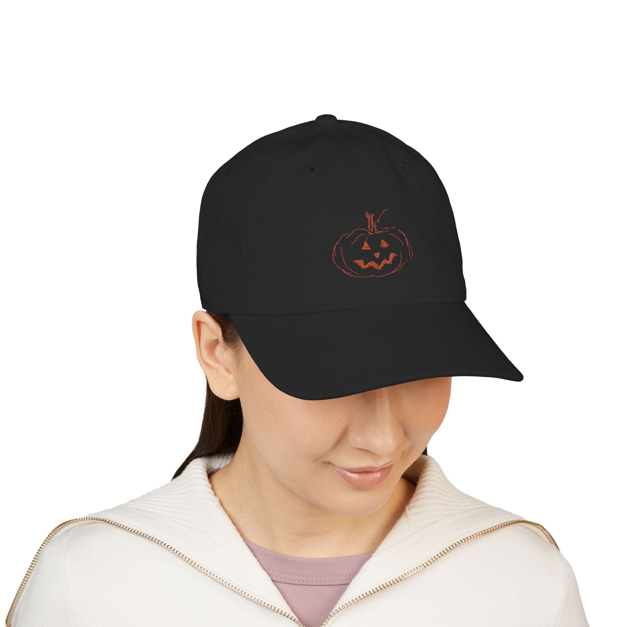 Female wearing a black baseball cap with embroidered jack-o-lantern pumpkin outline design on the front in a rusty orange color.